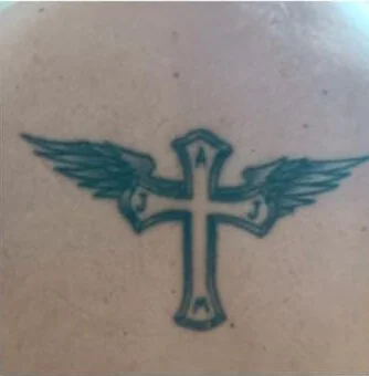 Tatuaje de cruz con alas en tinta azulada en la espalda antes del tratamiento láser